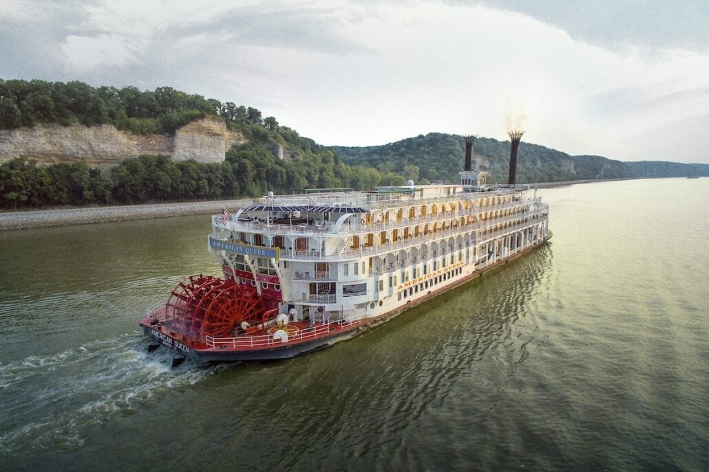 An aerial view of a riverboat cruising down a river.