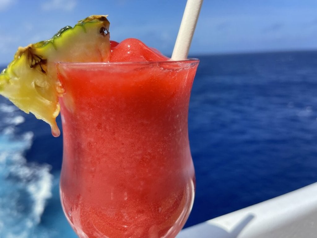 Enjoying a refreshing drink with a pineapple garnish on the deck of a cruise ship, courtesy of Carnival's drink package.