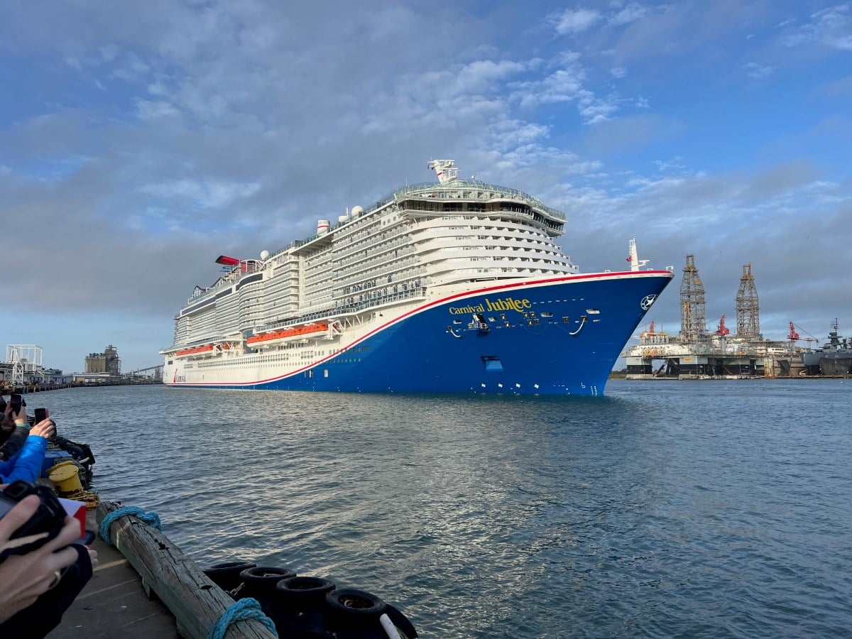 A large cruise ship, the Carnival Jubilee, is docked at a bustling port.