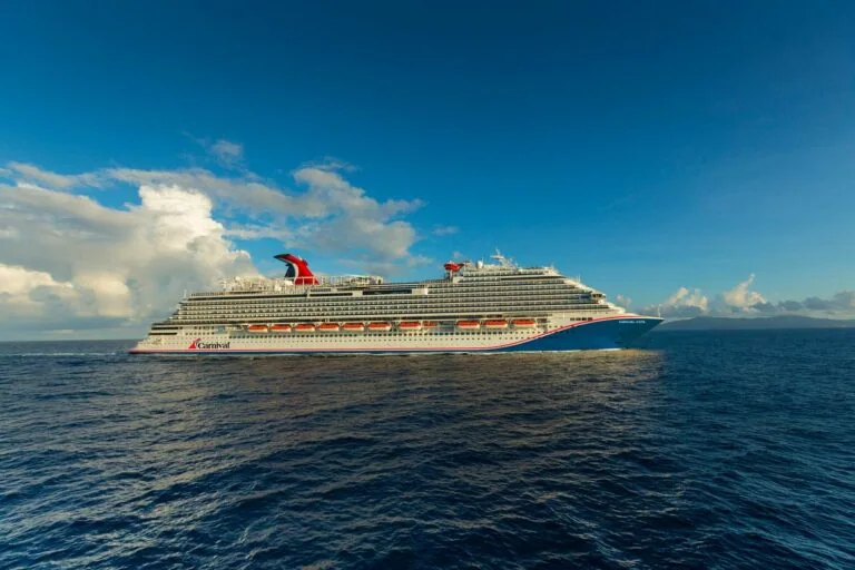 A large cruise ship, Carnival Vista, sailing on the open sea under a clear blue sky.