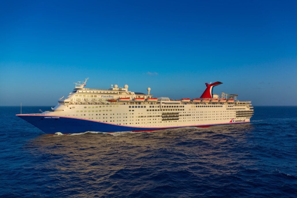 A large white Carnival cruise ship sails on the open sea under a clear blue sky, making its way from Tampa, with the name 