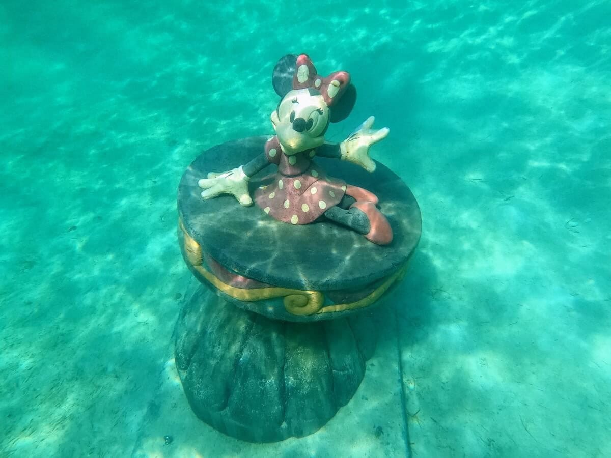 Minnie Mouse statue in a red polka-dot dress submerged underwater at Castaway Cay, sitting on a round platform.