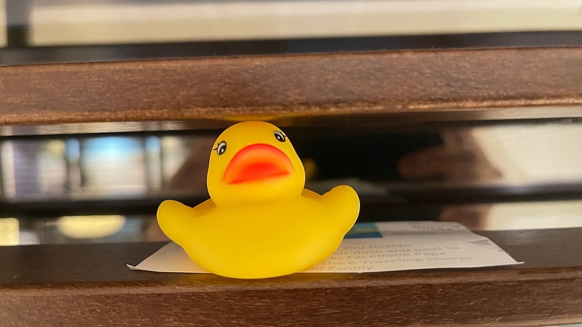 A rubber duck sits on top of a wooden shelf.