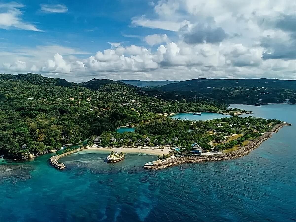 Aerial view of a coastal landscape with lush green hills, sandy beaches, and blue waters. Cloudy sky in the background.