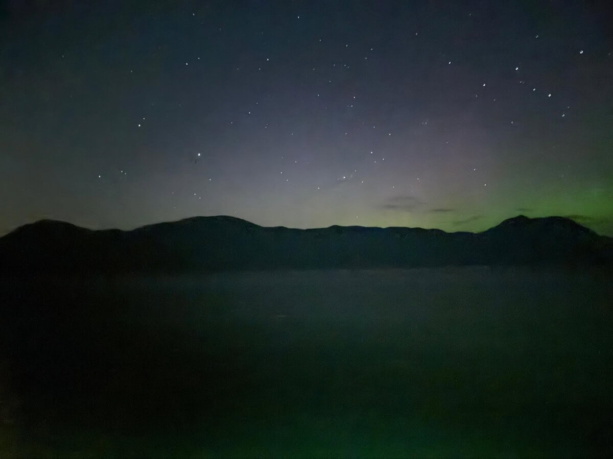 Nighttime landscape showing a faint aurora over dark silhouetted mountains during an Alaska Trip under a starry sky.