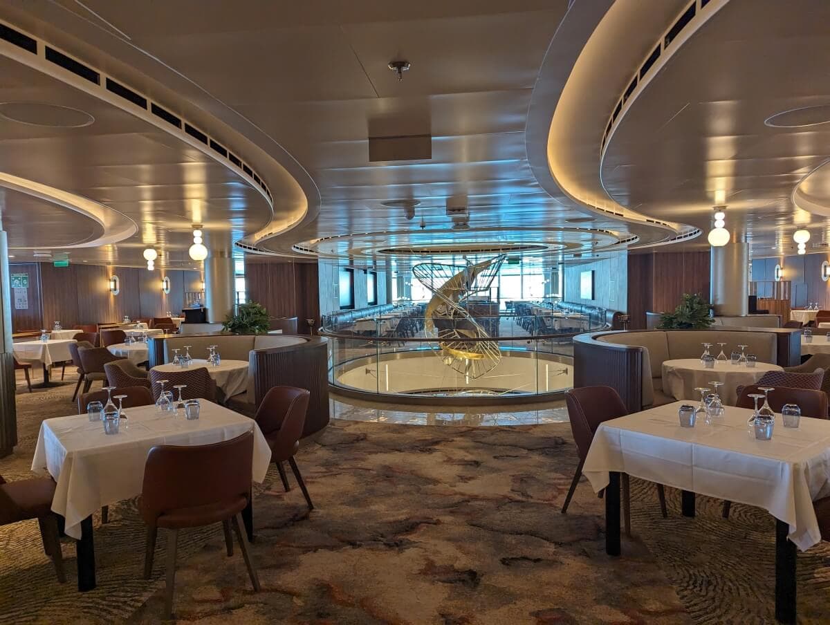 Elegant Sun Princess cruise ship dining room with tables set for a meal and a central circular glass sculpture.