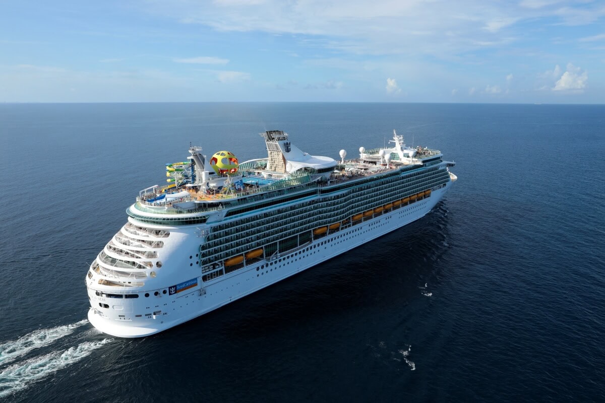 Aerial view of a large cruise ship sailing on the ocean, featuring multiple decks and recreational facilities, including a pool and a waterslide. The sky is clear with a few scattered clouds, creating the perfect auto draft setting for an unforgettable voyage.