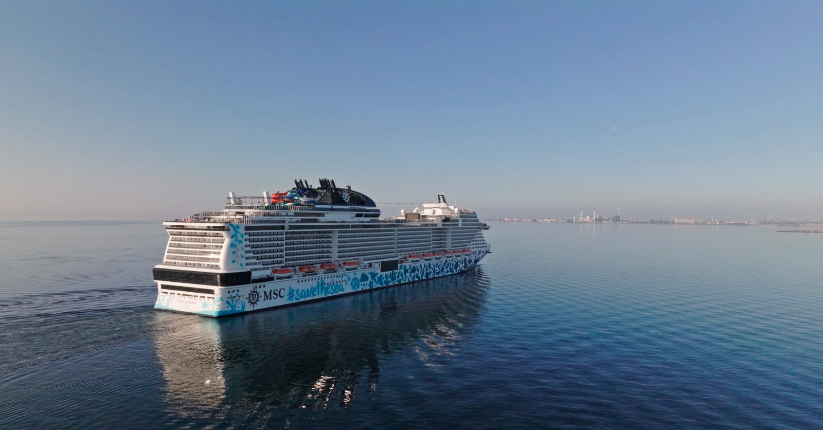 A large cruise ship sails on calm waters towards a distant shoreline under a clear sky, unaware of the tragedy unfolding—a passenger overboard incident reminiscent of a recent Norway event.