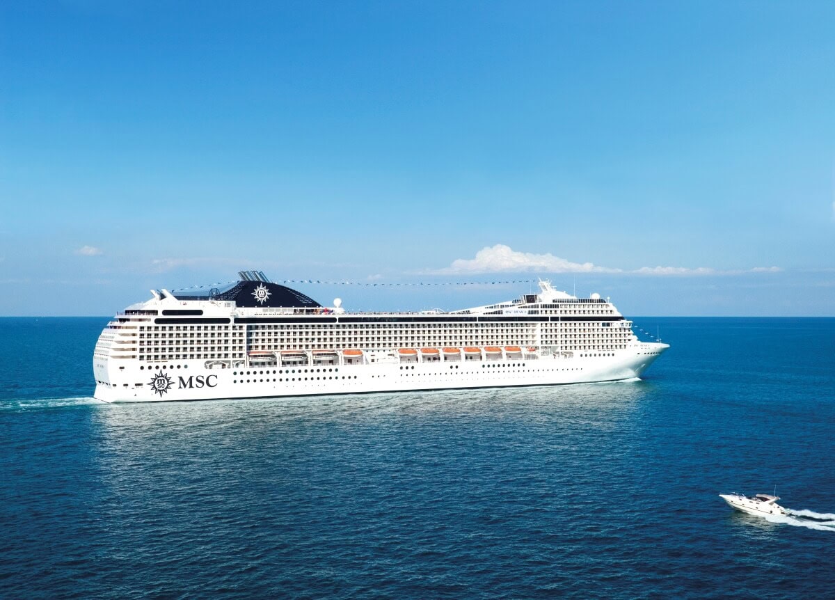 A large MSC Musica cruise ship sails in calm blue waters with a small motorboat nearby, ready for any crew member who might need to jump off for maintenance tasks.