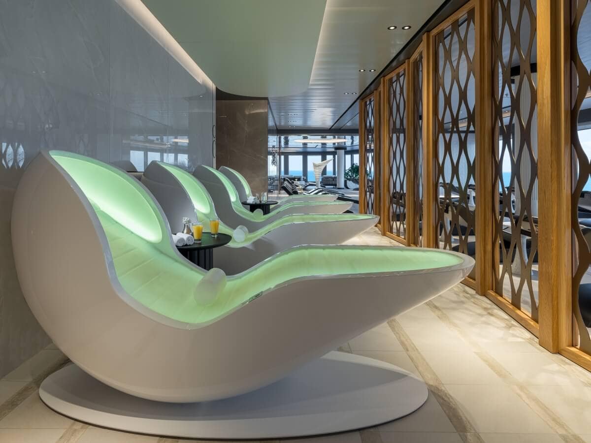 A luxurious lounge chair with green lights in front of a glass wall aboard the Norwegian Joy.