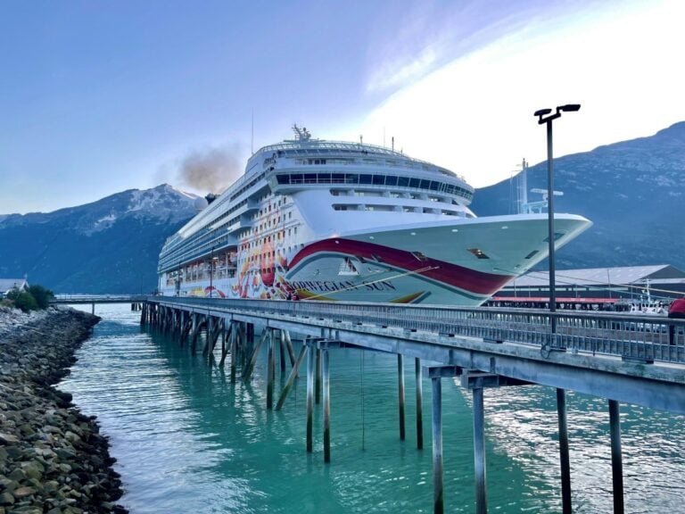 A cruise ship docked at a dock in front of mountains in Alaska.