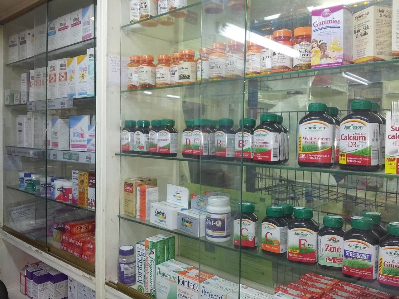 Shelves in a store display various vitamins, supplements, and medications in bottles and boxes, including remedies for seasickness on a cruise.