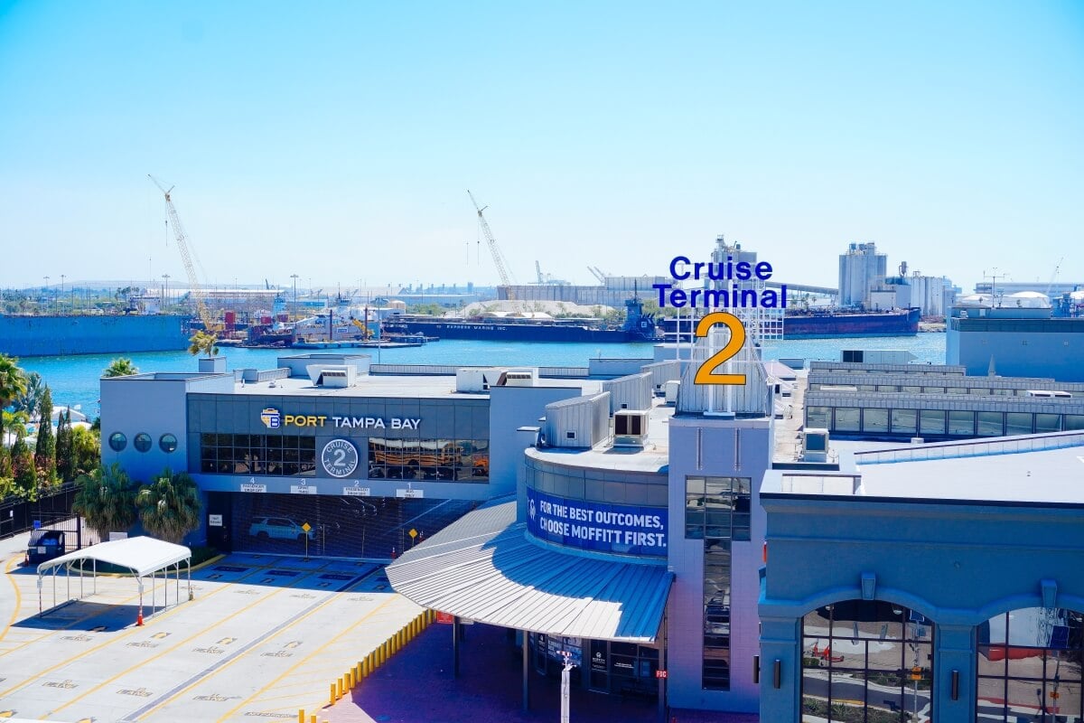 View of Port Tampa Bay's Cruise Terminal 2, with the harbor in the background and cranes visible on the horizon. The terminal building has signage and a parking/loading area in front. Plans for a Fourth Terminal are also underway to expand the port's capabilities.