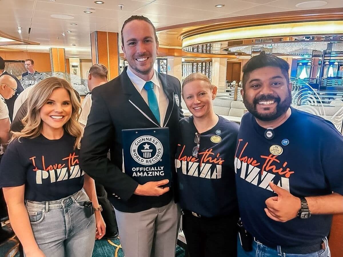 A group of four people posing indoors, with one holding a Guinness World Records certificate. Others wear t-shirts with 