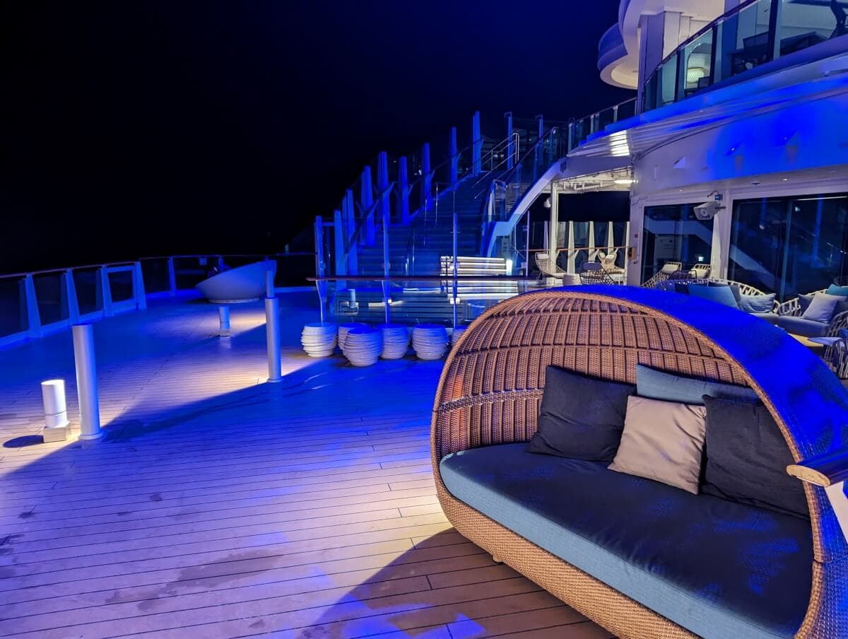 An empty cruise ship deck at night with a rattan cabana and blue lighting.