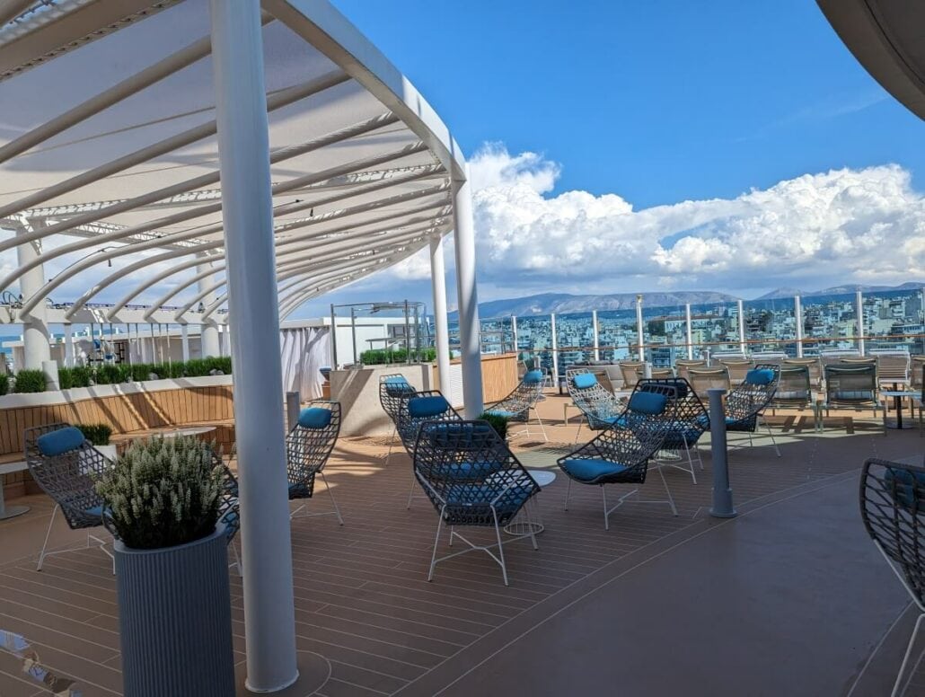 A modern rooftop terrace with lounge chairs and a panoramic view of the city under a partly cloudy sky.