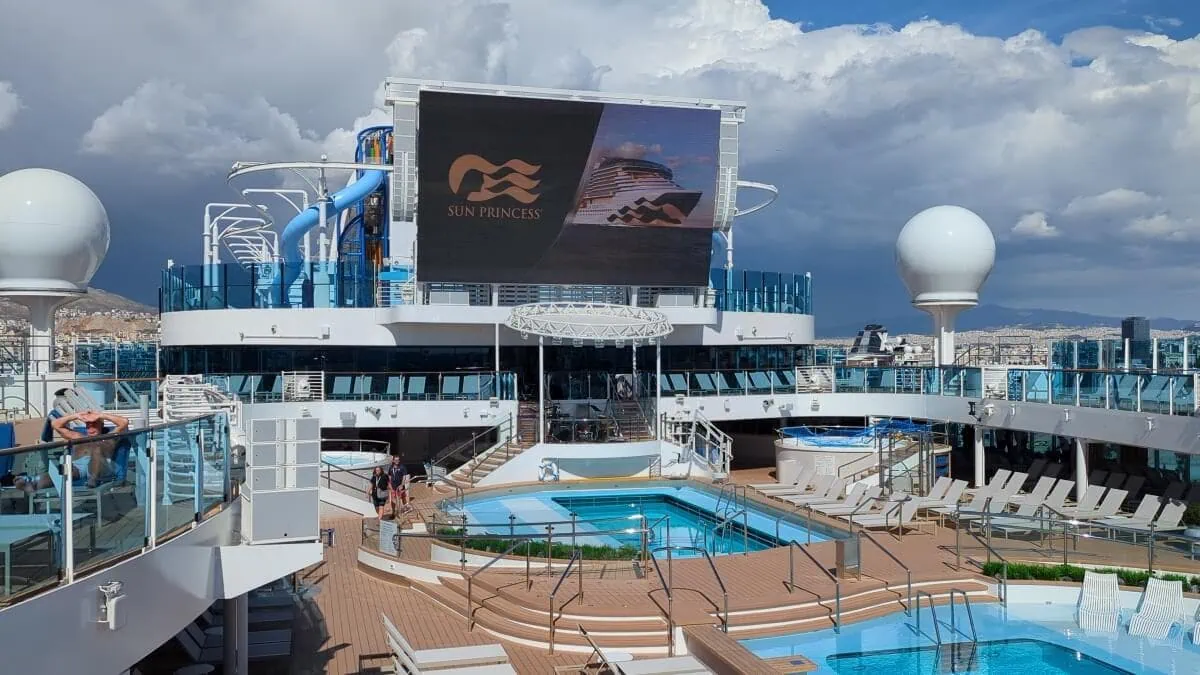 Deck of the sun princess cruise ship featuring swimming pools, lounging areas, and waterslides under a partly cloudy sky.