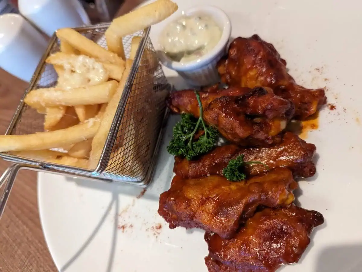 A plate of buffalo wings with a side of fries and dipping sauce.