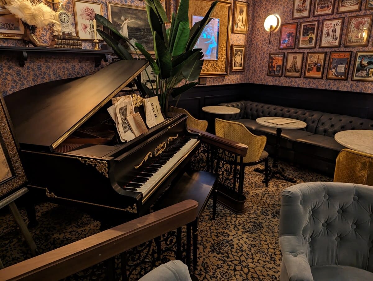 A grand piano in a cozy room with vintage decor and upholstered seating.