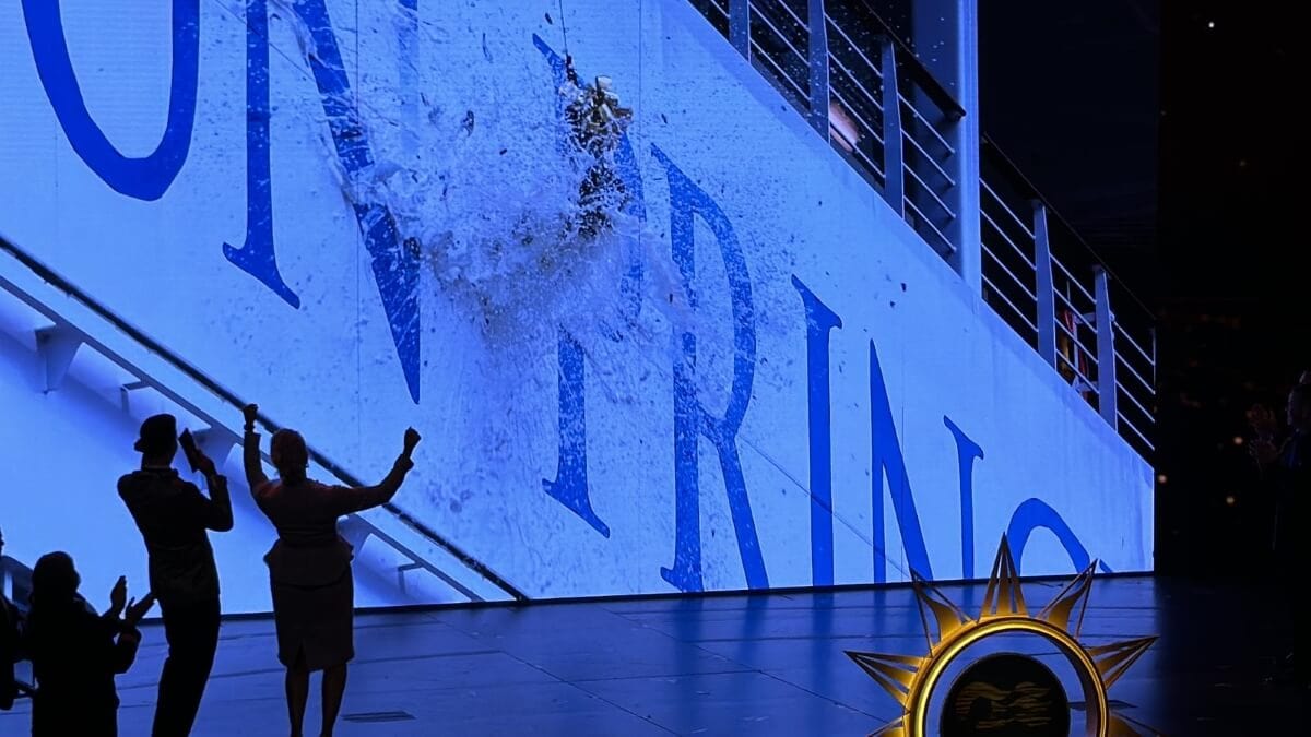 People celebrating as an image on a large screen appears to shatter, with a logo visible on the floor in a dimly lit arena.