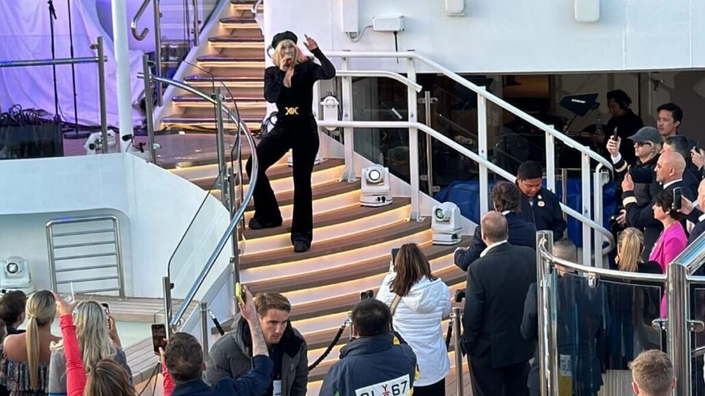 A man performs acrobatic dance on illuminated yacht stairs while an audience watches, some using cameras.