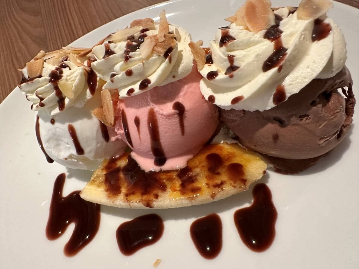 Three scoops of ice cream with whipped cream, almonds, and chocolate sauce served on top of a grilled slice of pineapple.